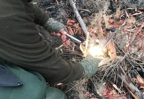 Choil of Bowie knife striking ferro rod for campfire.